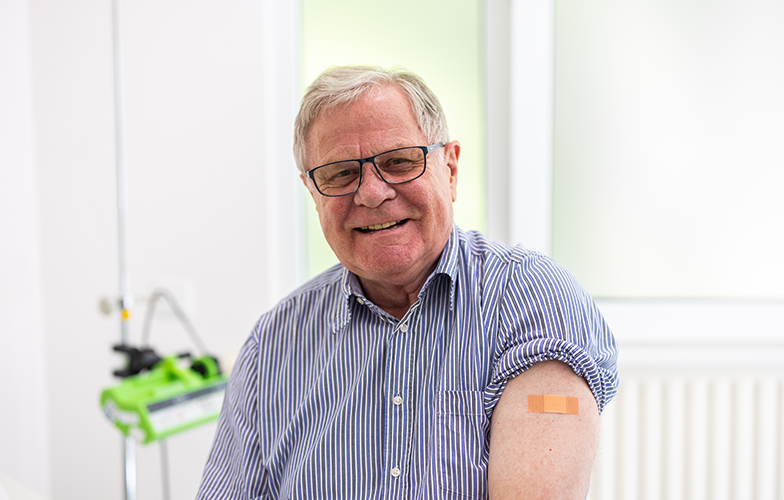 Happy old man showing vaccinated left arm with band-aid